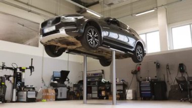 Araç, oto tamir atölyesinde hidrolik asansörde yükseltildi. Modern garajda araba bakımı ve teftişi. Atölyede hizmet ve onarım araçları görünür.