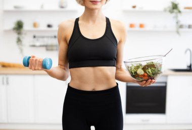 Modern mutfakta salata tutan atletik giysili formalı bir kadın. Sağlıklı yaşam tarzı egzersizini teşvik ediyor. Sağlıklı beslenme dengesini temsil eder.