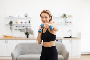 Atletik bir kadın, modern iç mekanlarda dambıllarla spor yapıyor, spor yaparken gülümsüyor, spor yapıyor, spor yapıyor ve sağlıklı bir yaşam sürüyor.