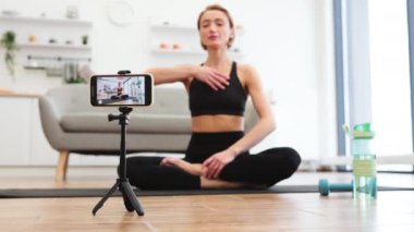Evde film çekerken yoga yapan bir kadın. Fitness, rahatlama ve farkındalık ile meşgul. Ev ortamı çalışma için barışçıl ve elverişli bir ortam yaratır..