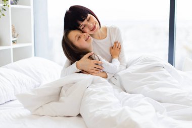 Anne ve kızı yatakta sarılıyor. Mutlu aile bağları ve samimi bir ortamda aşkla dolu aydınlık bir sabah. Evin rahatlığı ve sıcaklığı.