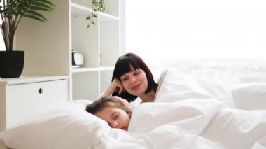 Anne ve çocuk beyaz çarşaflarda dinleniyor, sıcaklığını, sevgisini ve huzurlu aile ortamında aile bağlarını sergiliyor..