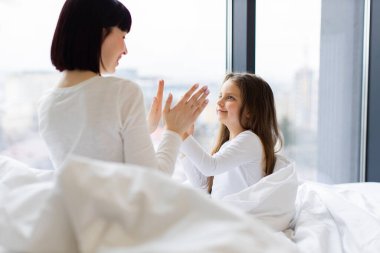 Anne ve kızı yatakta el çırpıyorlar. Rahatlatıcı bir sabahta ebeveynler ve çocuklar arasındaki mutluluk ve bağ. Parlak ve neşeli iç mekan.