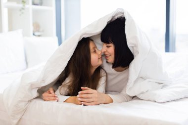 Sevgi, bağlılık ve mutluluğun hassas anlarını yakalamak. Anne ve kız yatakta yatıp oynuyorlar, evdeki gibi battaniyeyle kaplanmışlar..