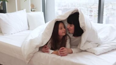 Sevgi, bağlılık ve mutluluğun hassas anlarını yakalamak. Anne ve kız yatakta yatıp oynuyorlar, evdeki gibi battaniyeyle kaplanmışlar..