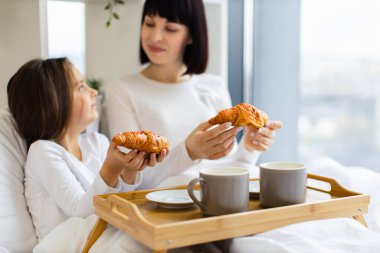 Anne ve kızı kahvaltıyı kruvasan ve kahveyle yatakta paylaşıyorlar. Gülümsüyor, kaynaşıyor ve kaliteli vakit geçiriyor. Sıcak sabah anı
