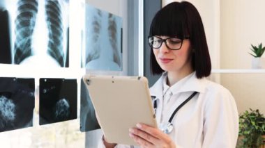 Gözlük takan ve laboratuvar önlüğü giyen kendine güvenen kadın doktor dijital tablette göğüs röntgenlerini inceliyor. Parlak ve modern klinik ortamında tıbbi uzman hasta sonuçları ve teşhislerine odaklandı.