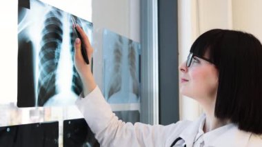 Beyaz önlüklü kadın doktor, ofisinde tabletle röntgen görüntülerini analiz ediyor. İçeride çalışan sağlık uzmanı, teşhis için hastanın tıbbi taramalarını inceliyor..