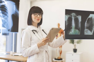 Doğru teşhis için sağlık uzmanı teşhis görüntülerini analiz ediyor. Modern klinikteki cam panoda tıbbi röntgenleri inceleyen kadın doktor. Doktor, hastanın göğüs röntgenlerini tablet kullanarak inceliyor..