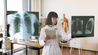 Kadın doktor cam panoda hastanın röntgenlerini inceliyor. Modern ofis ortamında profesyonel tıbbi danışma ve tanı analizi.