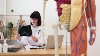 Laboratuar önlüklü bir tıp uzmanı ön planda insan vücudunun detaylı anatomik modeliyle röntgenini inceliyor. İnsan anatomisi, tıp ve sağlık bilimi eğitimi kavramı.
