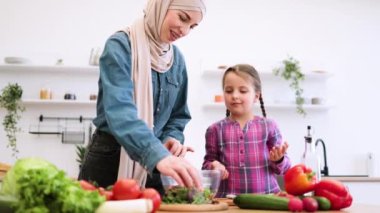 Müslüman anne-kız pirzola, salata kasesinde yeşillikler. Parlak, modern mutfakta sebze hazırlarken, sağlıklı beslenme ve yaşam tarzlarını sergilemekten zevk alıyorlar..