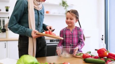 Mutfakta aile bağı. Müslüman anne ve kızı salata kasesine tahta tahtadan kesilmiş sebzeler döküyorlar. Sağlıklı yaşam tarzı ve besleyici yemek hazırlığı.