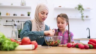Müslüman anne ve kızı modern mutfakta sağlıklı salatanın tadını çıkarıyorlar. Besleyici yiyecekler üzerine bağ kurmak, sevgi, mutluluk ve aile birliği duyguları yaratmak..