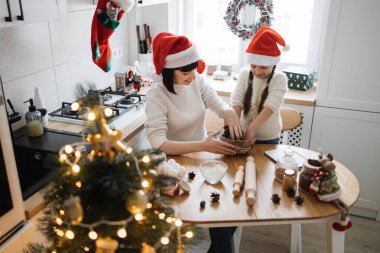 Kafkas anne ve küçük kızı, Noel için dekore edilmiş rahat mutfakta hamur yoğururlar. İkisi de Noel Baba şapkası takıyor, birlikte yemek pişiriyorlar..