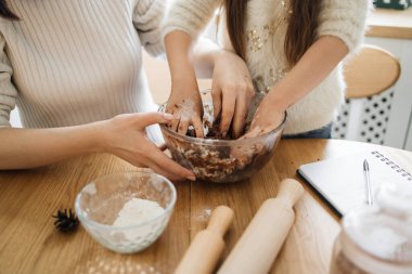 Anne ve kızı mutfak masasında hamur yoğuruyorlar. Ellerin un ve çikolata hamuruyla kirleniyor..