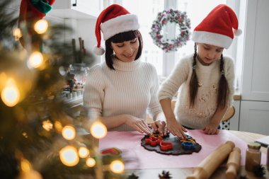 Kafkasyalı anne ve kız Noel Baba şapkası takıp birlikte kurabiye pişiriyorlar. Gülümseyen yüzler, tatil ruhunun sıcaklığı ve Noel zamanı ele geçirilen aile bağlarının neşesi..