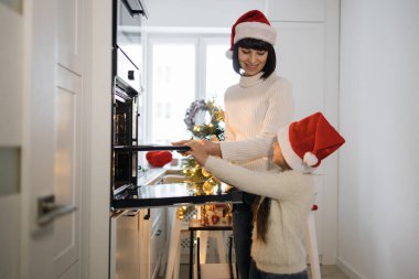 Kafkas anne ve küçük kızı Noel boyunca şapkalarını takıp kurabiye pişiriyorlar. Sıcak mutfak ortamında neşeli bir aile anı ve şenlikli dekorasyonlar..