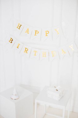 Altın harflerle yazılmış doğum günü afişi, mutlu yıllar, kurdeleli beyaz hediye kutusu, minimal beyaz arka planda parti şapkası, insan modeli yok.