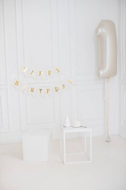 Minimalist doğum günü düzeneği Mutlu Yıllar pankartı, bir numara şeklinde gümüş balon, parti şapkası ve beyaz masa üzerinde mum olan pasta. Dekor neşe, kutlama ve sadelik taşır..