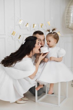 Annesi, babası, küçük kızı doğum gününü kutlayan beyaz bir aile. Anne, elinde iki numaralı pastayla şakacı bir şekilde, beyaz giyinmiş, meraklı görünümlü bir çocuk..