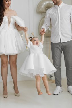 Farklı aileler tarafından kaldırılan beyaz elbiseli, gülümseyen genç kız. Zarif bir ortamda neşeli bir an yakaladık. Aile bağı ve mutluluk imajdan yayılıyor.