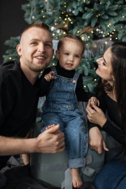 Kafkas aile portresi, genç ebeveynler ve yeni yürümeye başlayan bir kız Noel 'i kutluyor. Noel ağacının yanında oturan kızına sevgiyle gülümseyen ebeveynler..