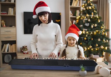 Kafkas anne ve kızı Noel 'i elektronik piyano çalarak ve birlikte Noel şarkıları söyleyerek kutluyorlar. Resim sıcak aile bağlarını, tatil ruhunu, müziğin neşesini yakalar.