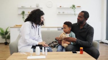 Afrikalı kadın doktor babasıyla evde otururken küçük çocuğa beşlik çakıyor. Sıcak etkileşim evde sağlık hizmetlerinde güven ve rahatlığı teşvik eder.