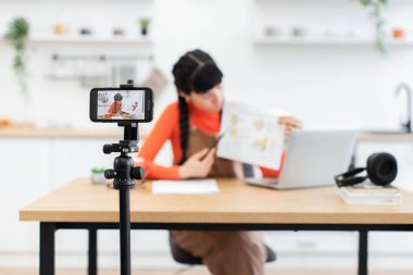 Beyaz kadın etkisinde eğitim içeriğini tripoda akıllı telefon kullanarak filme alan biri. Masasında dizüstü bilgisayar ve kitaplarla oturuyor. Parlak, havadar mutfaktaki kavramları anlatıyor..