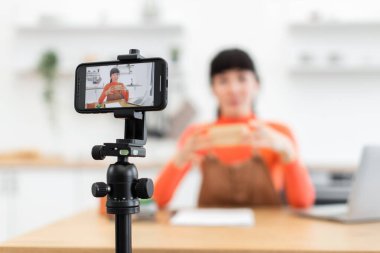 Mutfak kayıtlarındaki beyaz kadın blogcu akıllı telefon kullanarak boks videosu açıyor. Günlük giysiler giyiyor ve ürünlere verdiği gerçek tepkileri paylaşıyor. Kamera canlı içeriği yakalayan telefon ekranına odaklanıyor.