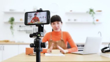 Kafkas kadın blogcu modern mutfakta boks videosu açıyor. Genç bir kadın üç ayaklı akıllı telefon kamerasıyla ürün incelemesini paylaşıyor. İçerik oluşturma ile çevrimiçi izleyiciyi meşgul et.
