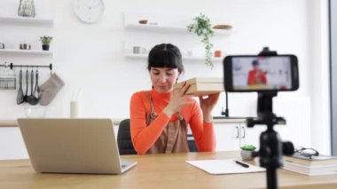 Beyaz kadın blogcu, yeni akıllı telefonları hevesle açıyor. Masada kamera ve dizüstü bilgisayarla video kayıt cihazı var. Vurgulama teknolojisi, çevrimiçi varlık ve modern iletişim.