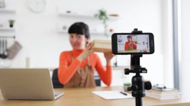 Parlak kıyafetli beyaz kadın çevrimiçi boks videosunda yeni bir akıllı telefon gösteriyor. Aygıt kamerada belirgin bir şekilde görüntülenir, içeriği yakalar.