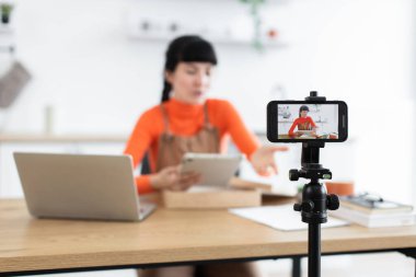 Beyaz kadın blogcu çevrimiçi izleyiciler için dijital tablet açıyor. Genç bir kadın canlı yayında izleyicileri kendine çekiyor. Bilgisayarlı ev stüdyosu kurulumu, akıllı telefon kamerası içerik oluşturma görüntüsü.