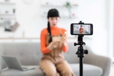 Beyaz kadın blogcu, çevrimiçi video kaydedilirken karton kutuda hediyesini açıyor. Genç kadın, izleyicilerle deneyimi paylaşmaya odaklanmış, kanepede oturuyor..