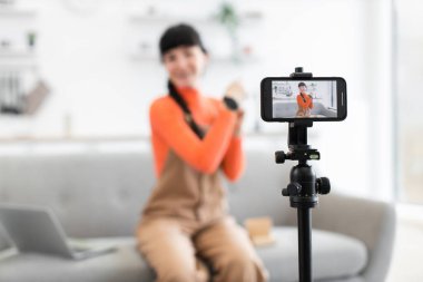 Kafkas kadın blogcu modern oturma odasındaki karton kutudan akıllı saati çıkarıyor. Kanepeye oturmuş, turuncu bir bluz ve tulum giyiyor. Akıllı telefon tripod kurulumu kullanılarak kayıt işlemi.