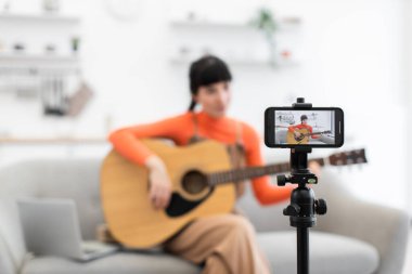 Beyaz kadın blogcu evde online gitar videosu kaydediyor. Genç yetişkin gitar eğitmeni müzik tutkunları için ilgi çekici içerik oluşturuyor.