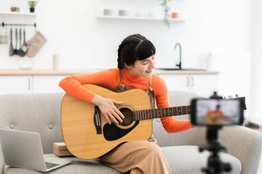 Kafkas kadın blogcu, 20 'li yaşlarda evde akustik gitar çalmak üzerine çevrimiçi video kursu kaydediyor. Kanepede gitarla oturuyor, kamera dersini kaydediyor..