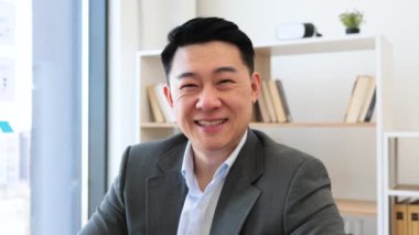 Ofis ortamında resmi giyinmiş Asyalı erkek işadamının portresi. Masasında oturmuş dizüstü bilgisayarla çalışıyor, kendine güveni ve profesyonelliği yayıyor..