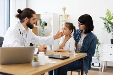 Tıbbi konsültasyon sırasında annesi doktor muayenehanesinde beyaz bir kız. Kadın doktor, sağlık sorunlarını tartışırken çocuğu muayene ediyor.