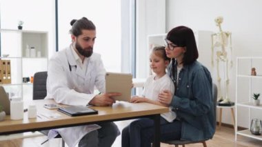 Kafkas erkek doktor modern klinikteki beyaz anne ve kızına test sonuçları gösteriyor. Anne ve çocuk dikkatle dinlerken doktor tedavi seçeneklerini açıklıyor..