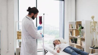 Erkek doktor, hastane yatağında yatan genç kıza kan nakli yapıyor. Beyaz önlüklü bir doktor, sakin görünen bir kızın yanında duruyor..