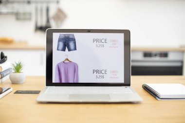 İndirimli kıyafet satan internet mağazasını gösteren bir laptop aç. Fiyatlarla gösterilen kot pantolon ve süveter gibi çeşitli giyim ürünleri. Sahne modern online alışveriş ve dijital ticareti öneriyor.