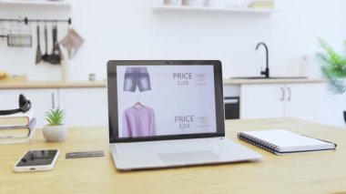 İndirimli kıyafet satan internet mağazasını gösteren bir laptop aç. Fiyatlarla gösterilen kot pantolon ve süveter gibi çeşitli giyim ürünleri. Sahne modern online alışveriş ve dijital ticareti öneriyor.