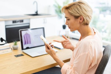 Ofisteki beyaz bir kadın online alışveriş konusunda müşteri hizmetlerini ayarlıyor. Sıradan kıyafetler giymek, telefonda hayal kırıklığını ifade etmek. Sahne, modern e-ticaretin ve etkileşimin özünü yakalıyor