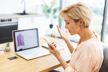 Beyaz bir kadın internet üzerinden kıyafet siparişi meselesini konuşmak için telefonla konuşurken hayal kırıklığını dile getiriyor. Dizüstü bilgisayarı satın alınan eşyaların endişelerini doğruluyor.