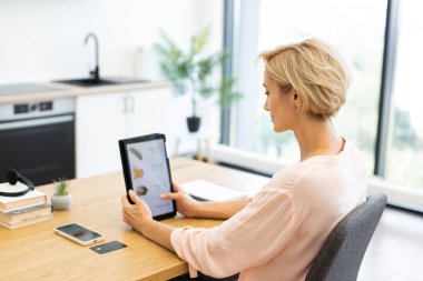 Modern ev ortamında yemek sipariş etmek için tablet kullanan beyaz bir kadın. Günlük sahne, dijital teknolojinin günlük yaşamı geliştirdiğini gösteriyor.