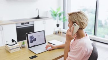Beyaz bir kadın telefon ve dizüstü bilgisayarla internetten kıyafet sipariş ediyor. Teslimat sitesine göz atıyor ve banka kredi kartıyla ödeme yapıyor. E-ticaret ve çevrimiçi alışveriş kavramları için ideal..