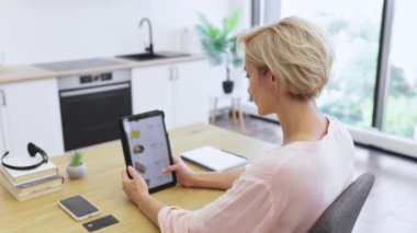 Modern ev ortamında yemek sipariş etmek için tablet kullanan beyaz bir kadın. Günlük sahne, dijital teknolojinin günlük yaşamı geliştirdiğini gösteriyor.